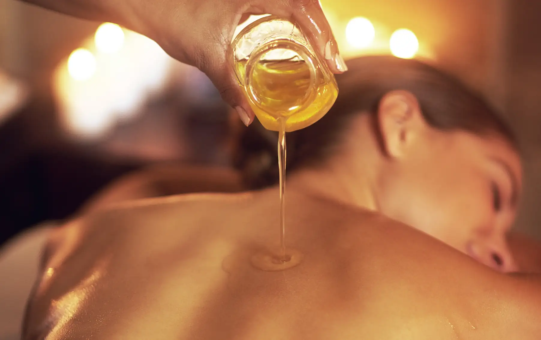 A close-up of a herbal oil slowly dripping onto a client’s back as she relaxes and prepares to receive her Oil bath.