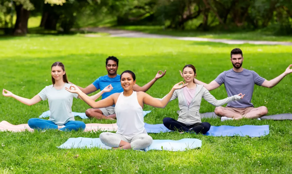 Group meditating outdoors as part of Ayurvedic daily routine to reduce stress