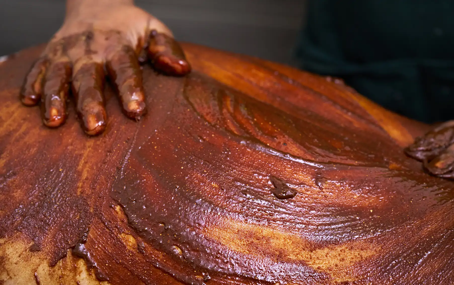 A close-up shot where a herbal paste is applied by hand onto a client’s body in a rhythmic pattern.