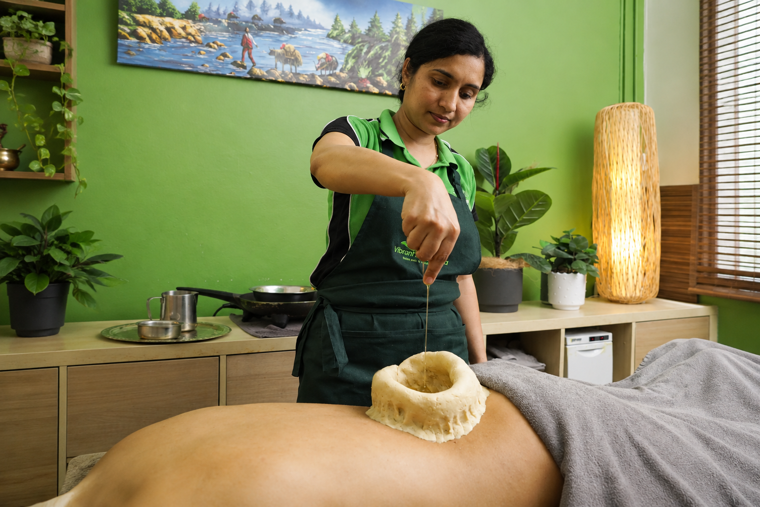 Ayurvedic therapist pouring warm oil into dough ring on client’s back at Vibrant Ayurveda.