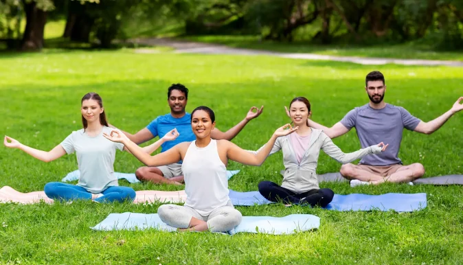 Group meditating outdoors as part of Ayurvedic daily routine to reduce stress